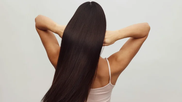 Achteraanzicht van een vrouw in een wit hemdje met haar armen omhoog, terwijl ze haar vingers door haar lange, glanzende donkerbruine haar haalt
