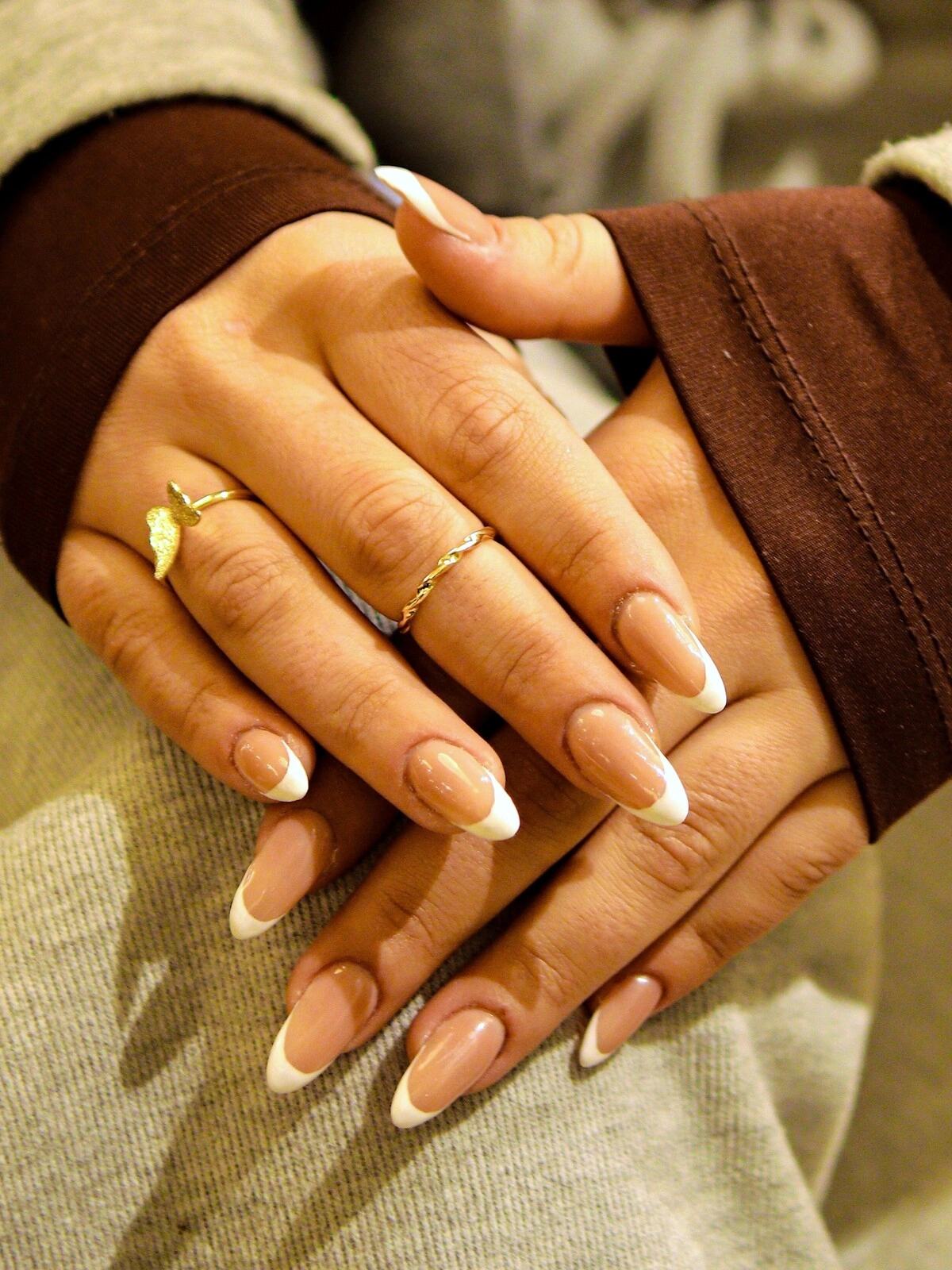 De handen van een vrouw met een opvallende French manicure in een combinatie van beige en wit op lange, amandelvormige nagels
