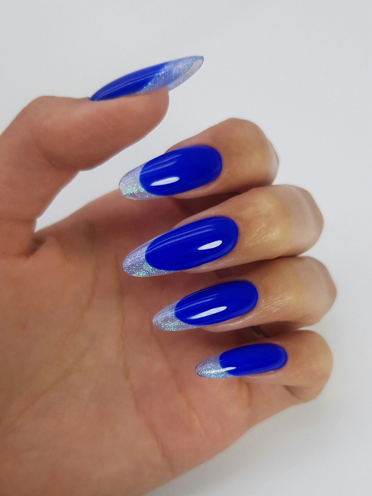 De hand van een vrouw met een opvallende French manicure met een felblauwe basis en zilveren metallic tips op lange, amandelvormige nagels
