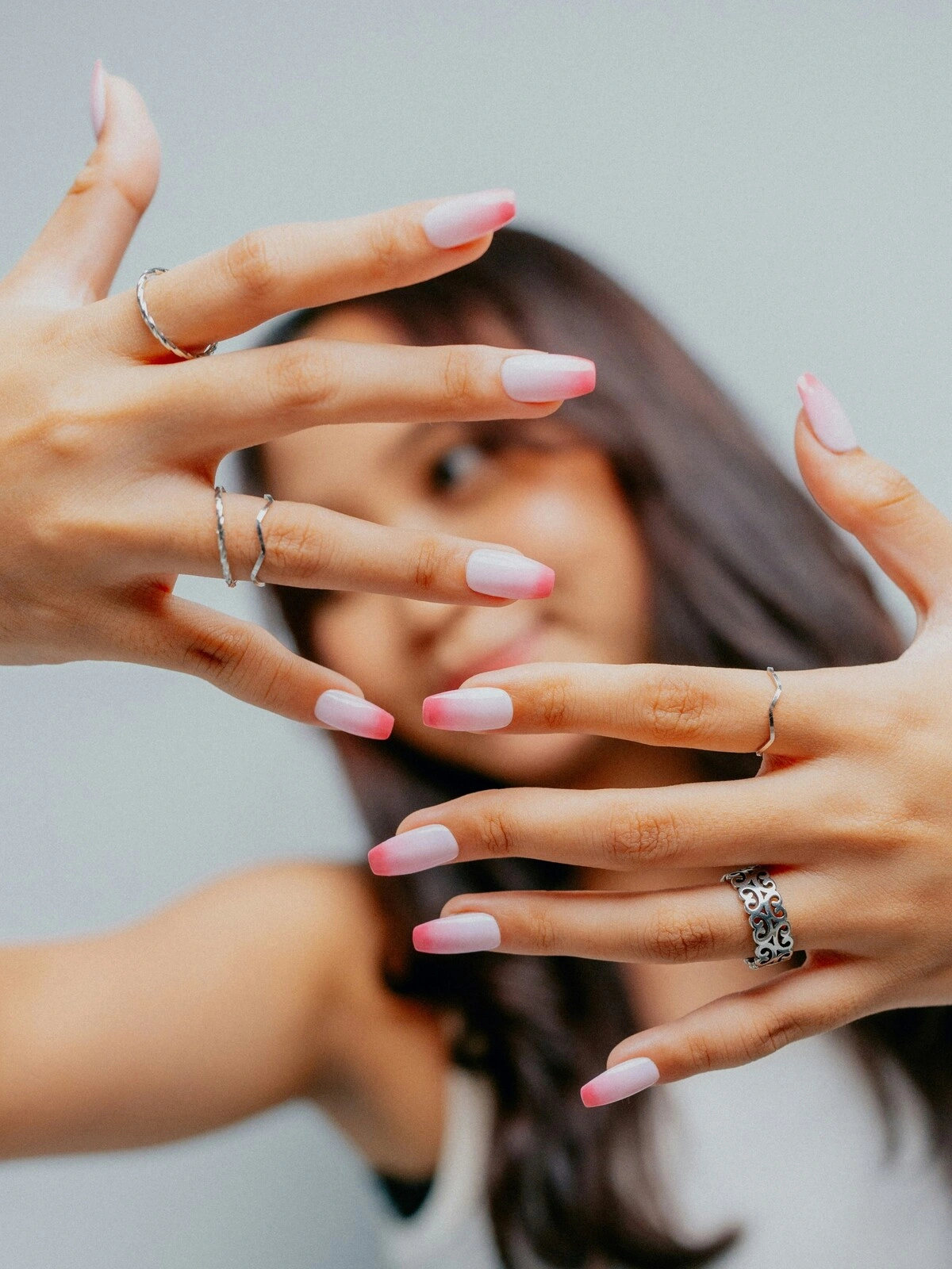 Een vrouw houdt haar handen naar de camera en toont een French manicure in ombre-look met een lichtroze basis en felroze tips op ballerinanagels