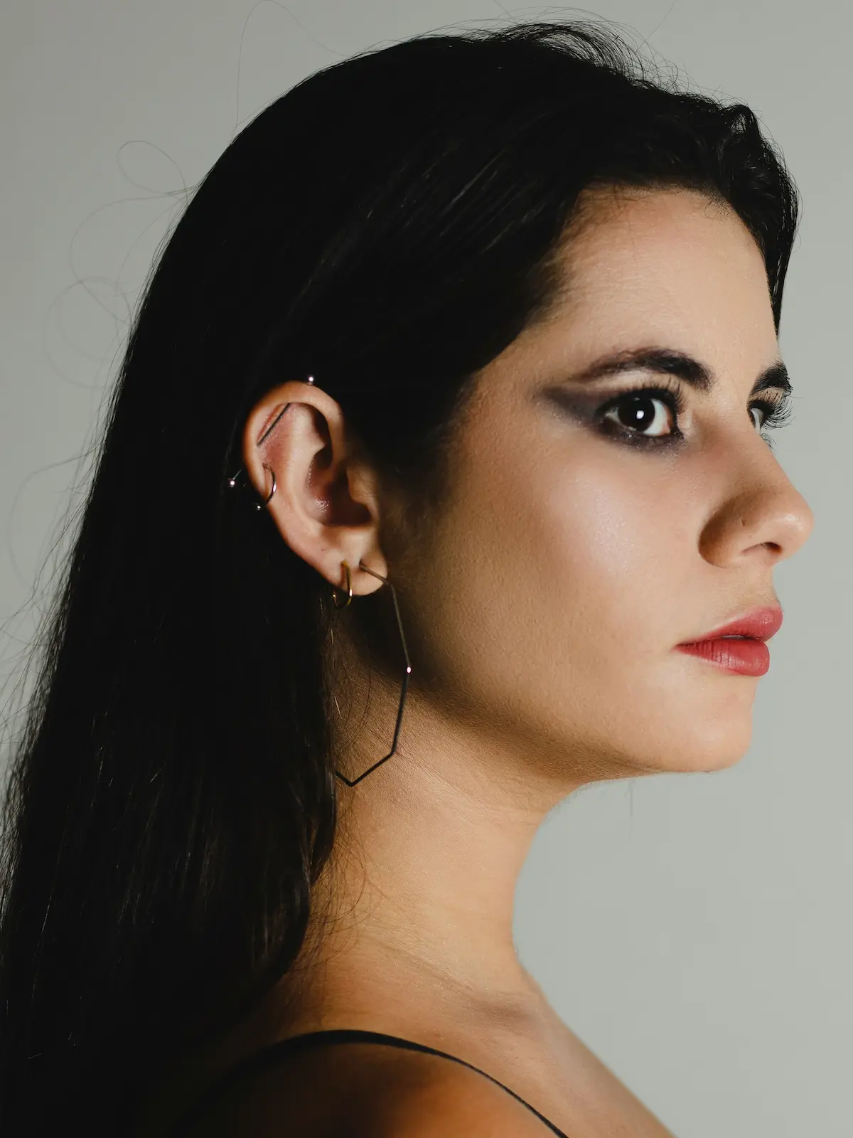 Studiofoto van een vrouw met een industrial barbell, oorlel- en helixpiercings