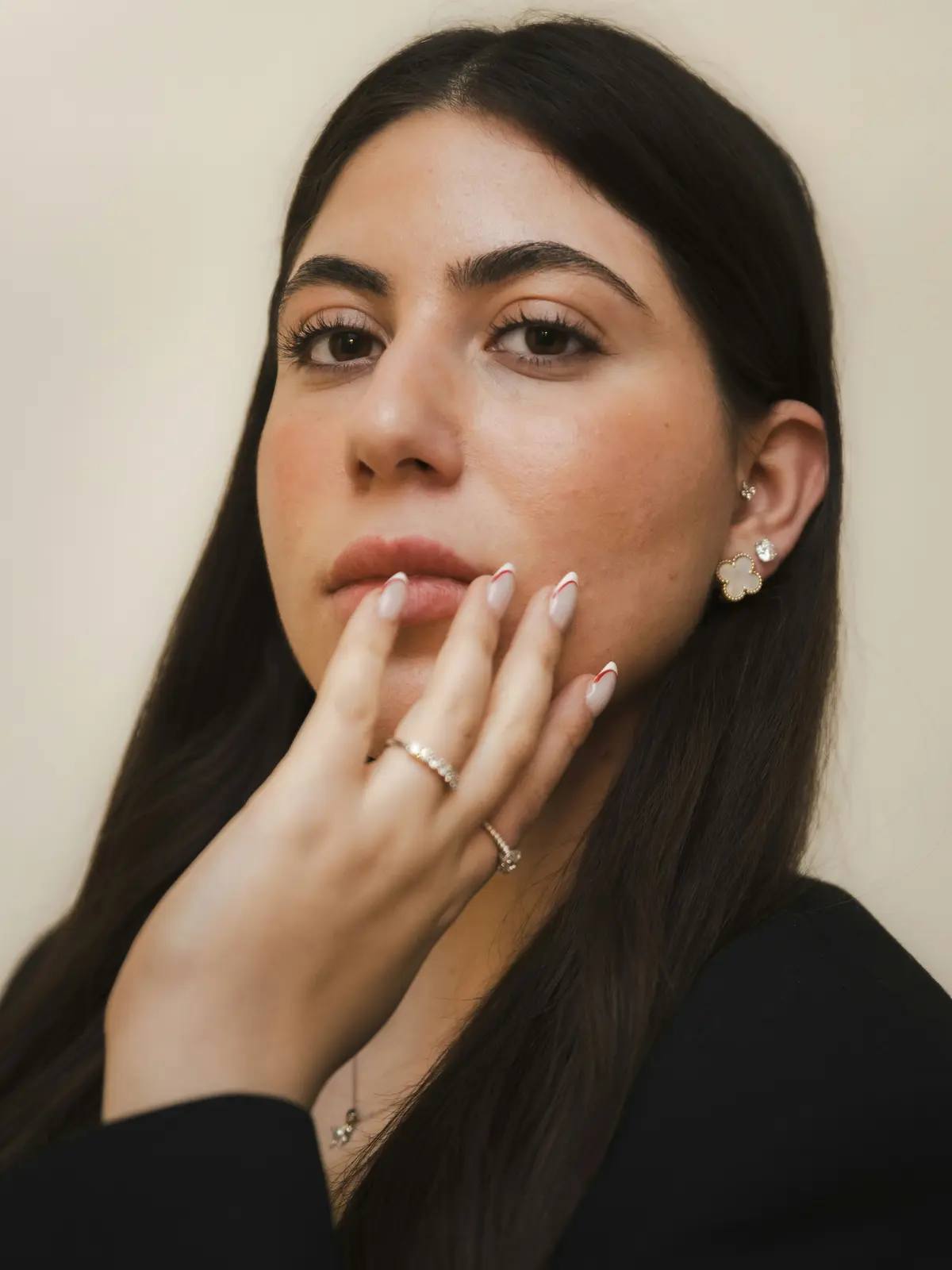 Studiofoto van een vrouw met oorlel- en traguspiercings die een gemanicuurde hand bij haar gezicht houdt