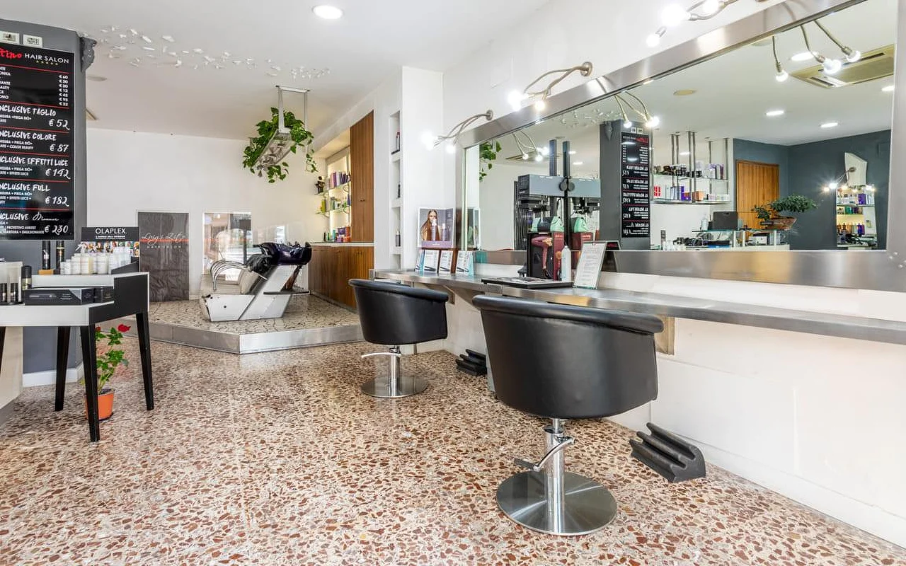 Het interieur van Hair Salon Luigi Zito, met terrazzovloer, twee zwarte stylingstoelen voor een lange spiegel, prijsborden van krijt aan de muur, een productdisplay en een wasbak achterin.