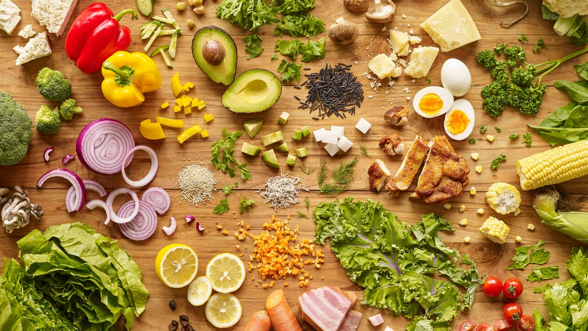 Bovenaanzicht van een houten aanrecht met kleurrijke, gezonde voeding, waaronder eieren, groenten, salade en kip