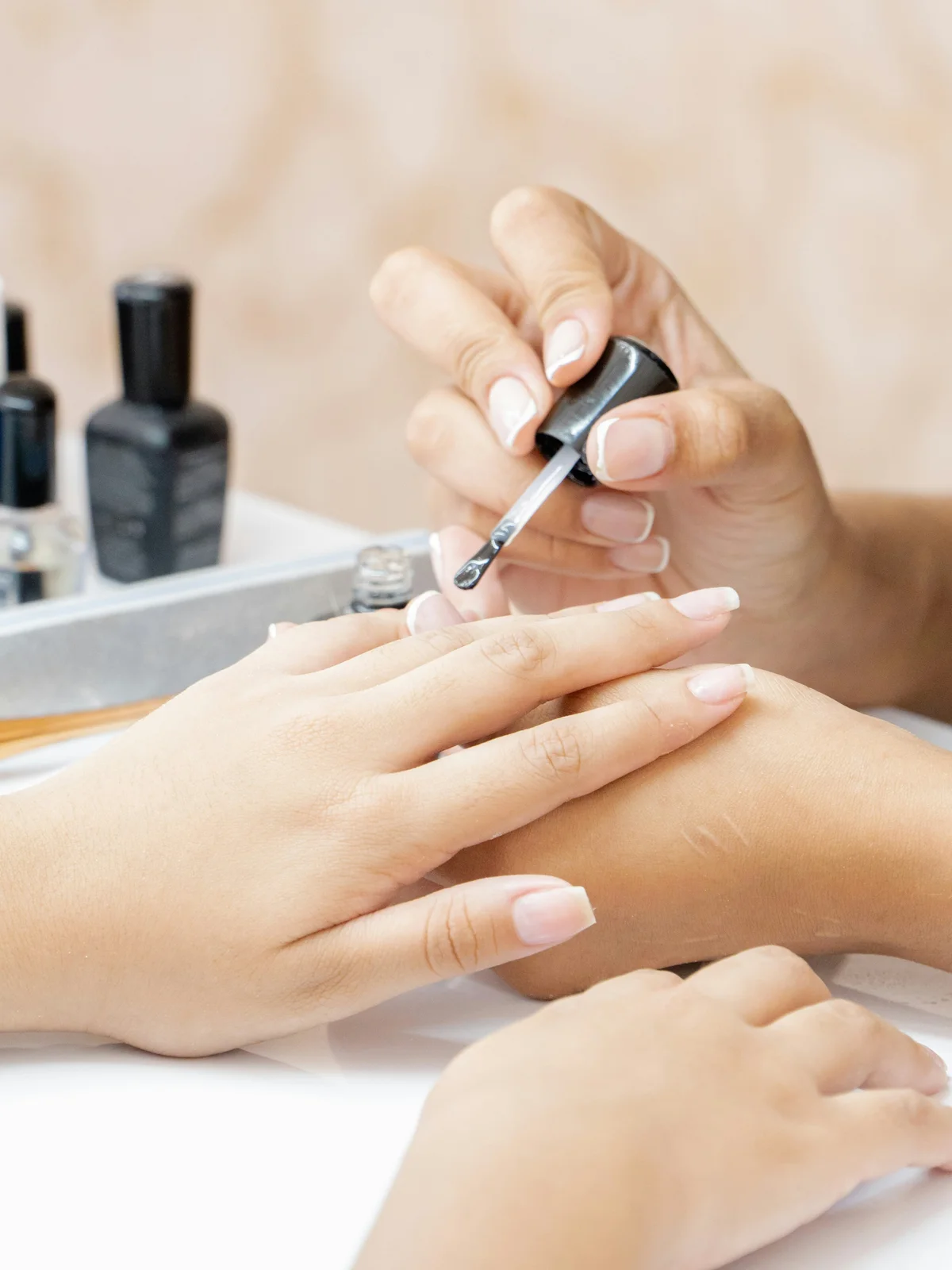 Close-up van een stylist die een transparante versterkende behandeling aanbrengt op de nagels van een klant in een salon