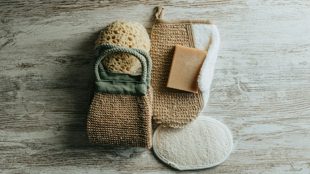 Flatlay met scrubhandschoenen, een natuurspons en een scrubzeep