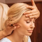 Close-up van een vrouw met haar ogen dicht terwijl een specialist tijdens een Indische hoofdmassage een hand op haar voorhoofd legt en met de andere hand haar nek masseert