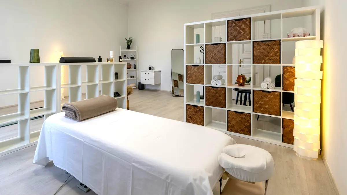 Een schone, opgeruimde behandelkamer in een salon met een opgemaakte behandeltafel en een opgerolde deken, klaar voor een massagebehandeling