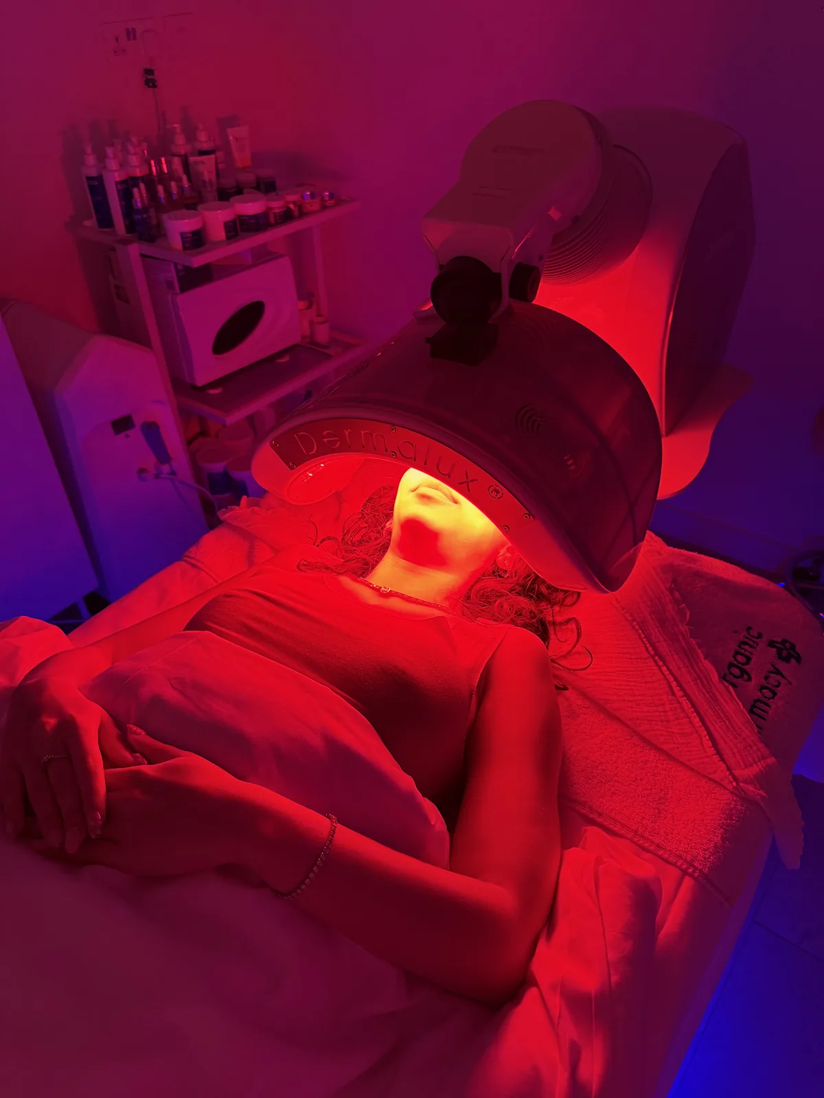 Vrouw ontspant onder een rood ledlichtpaneel tijdens een spabehandeling